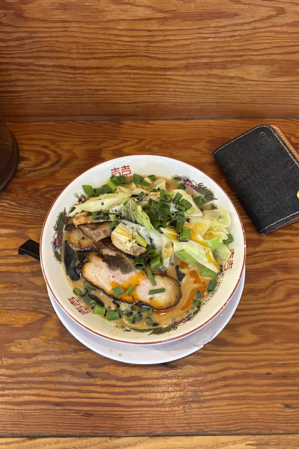 Bowl of ramen with pork, cabbage and scallions on a wooden counter