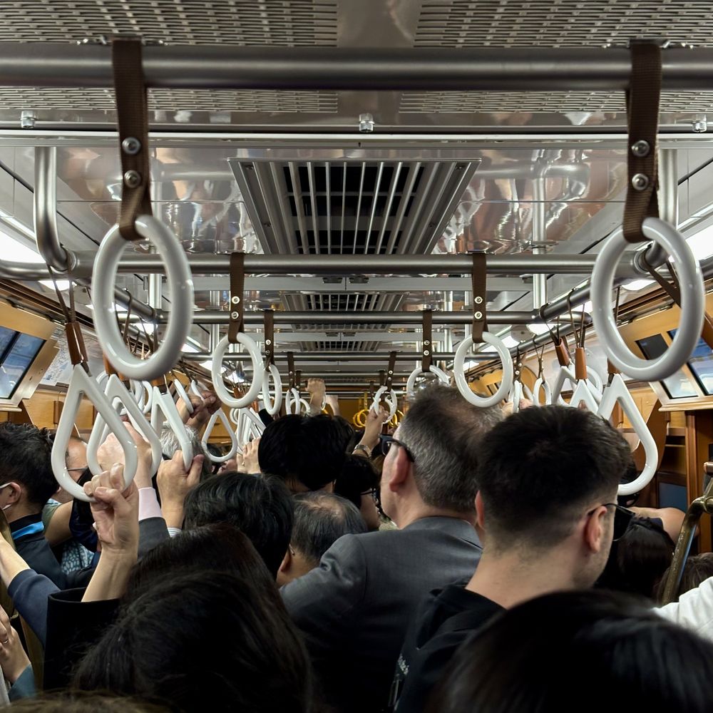 Crowded train with white hanging straps and commuters seen from behind
