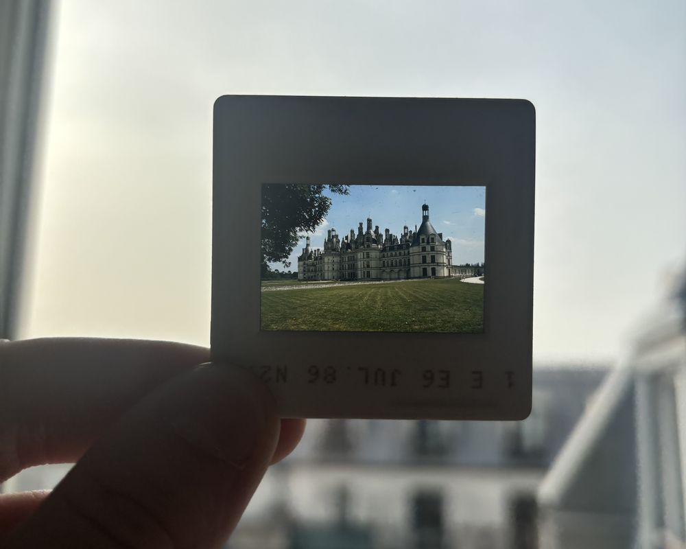 Hand holding a film slide that shows a large chateau against a bright sky