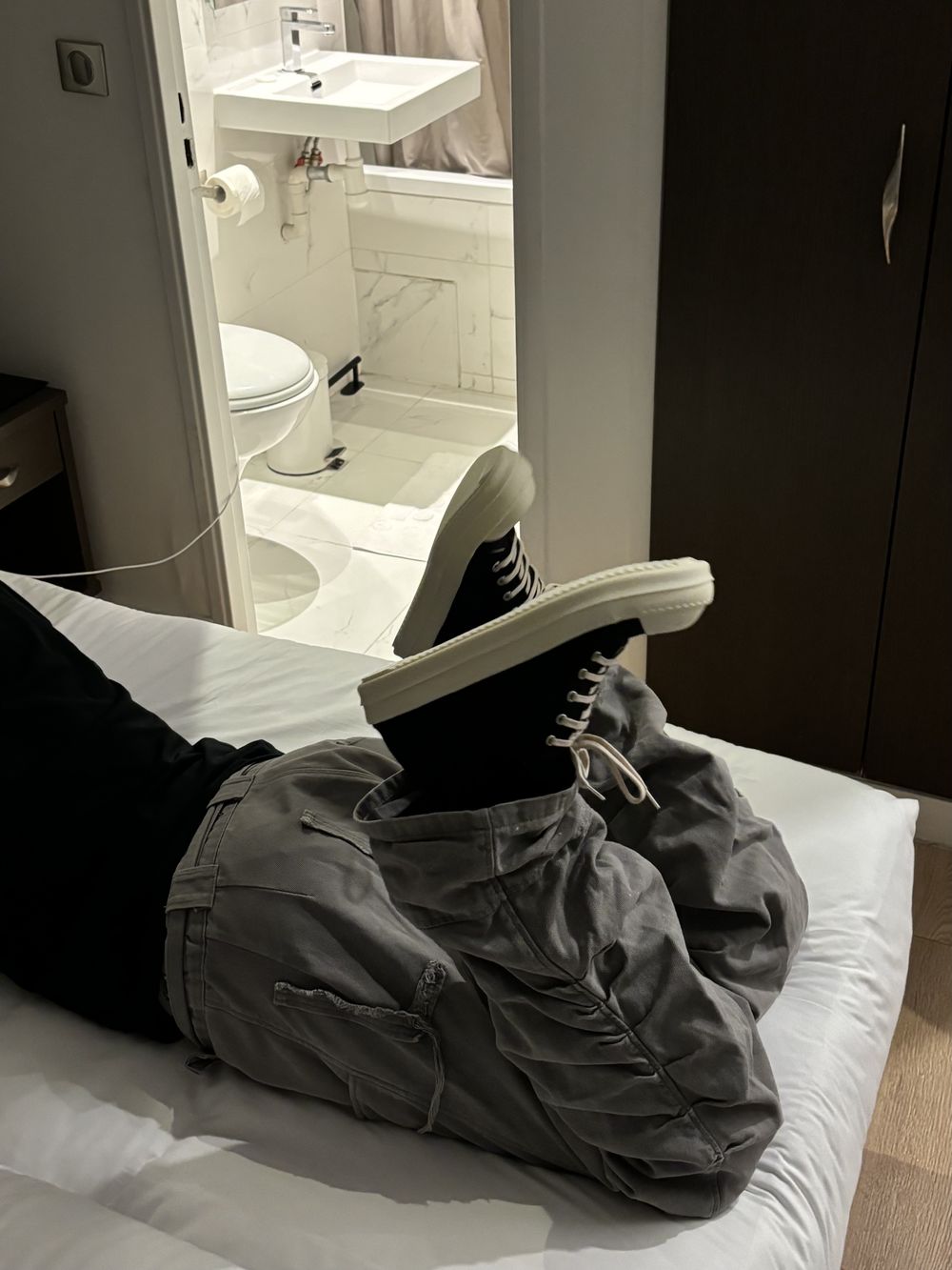 Person lying on a bed with sneakers up in the air, bathroom in the background