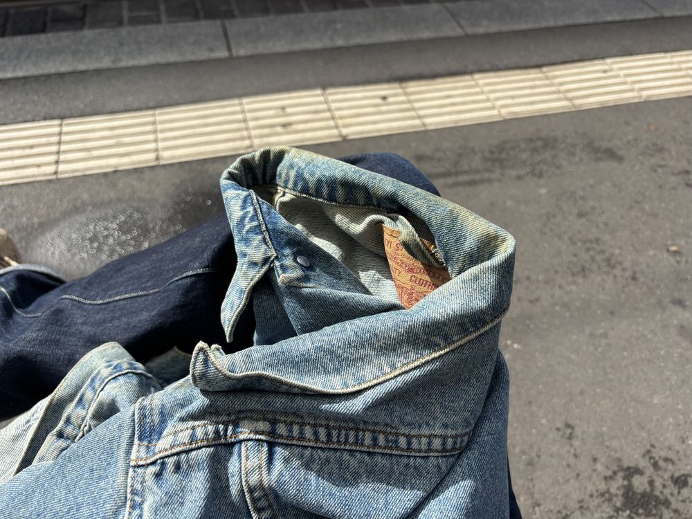 Worn denim jacket with a folded collar lying on the ground next to tactile paving