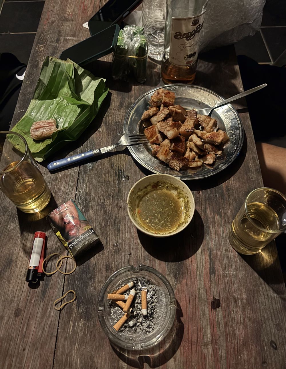 Table with plates of food, drinks, a lighter and an ashtray