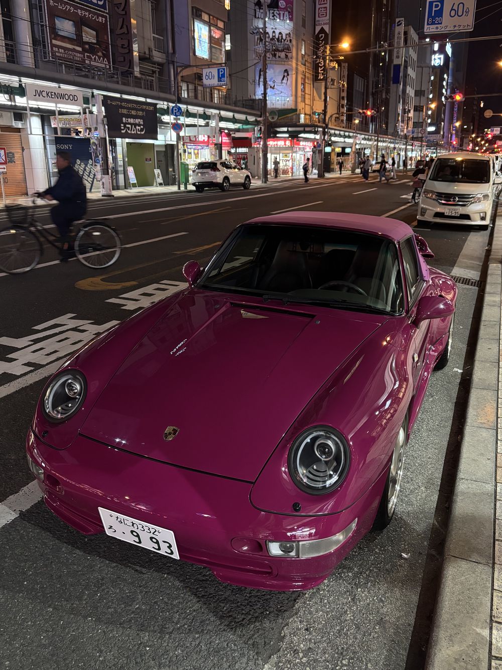 Magenta Porsche 911 parked on a Japanese street at night with a cyclist behind it