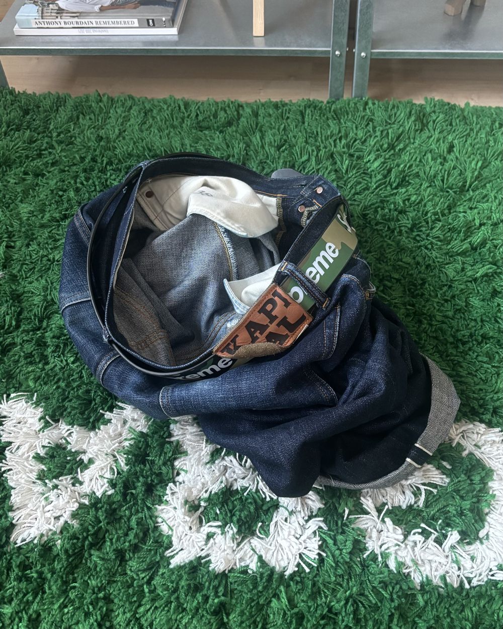 Dark denim jeans lying on a green fuzzy rug with white lettering
