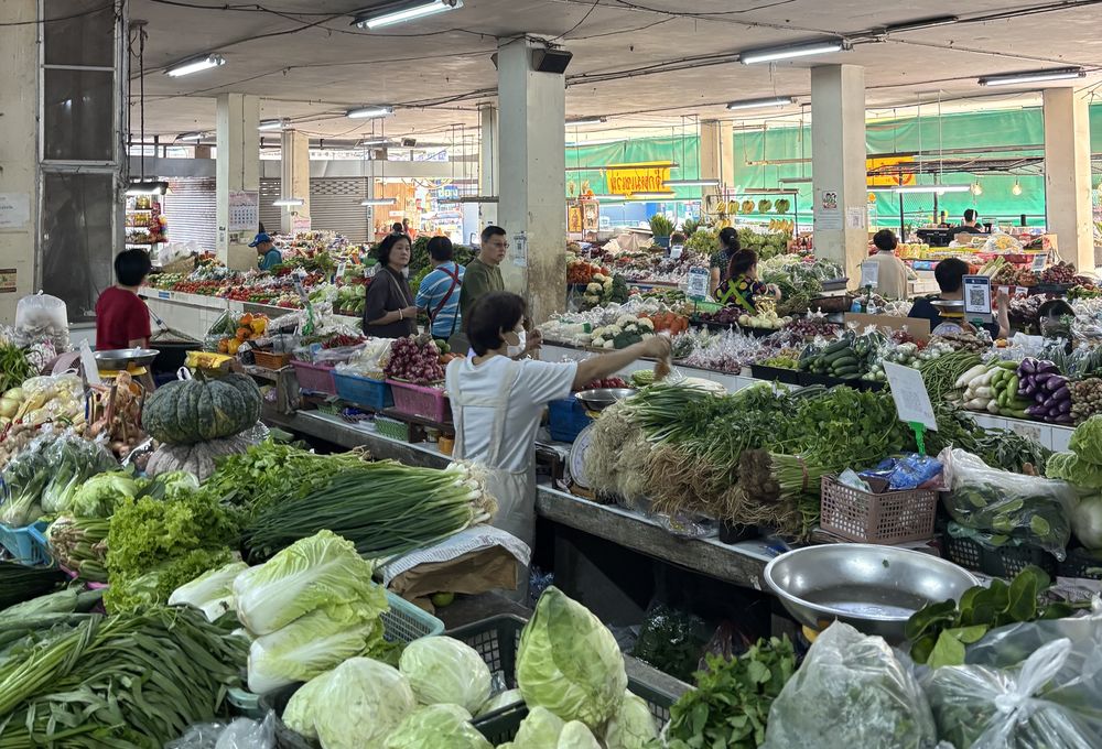 Indoor market hall with stacks of green vegetables and shoppers in the background